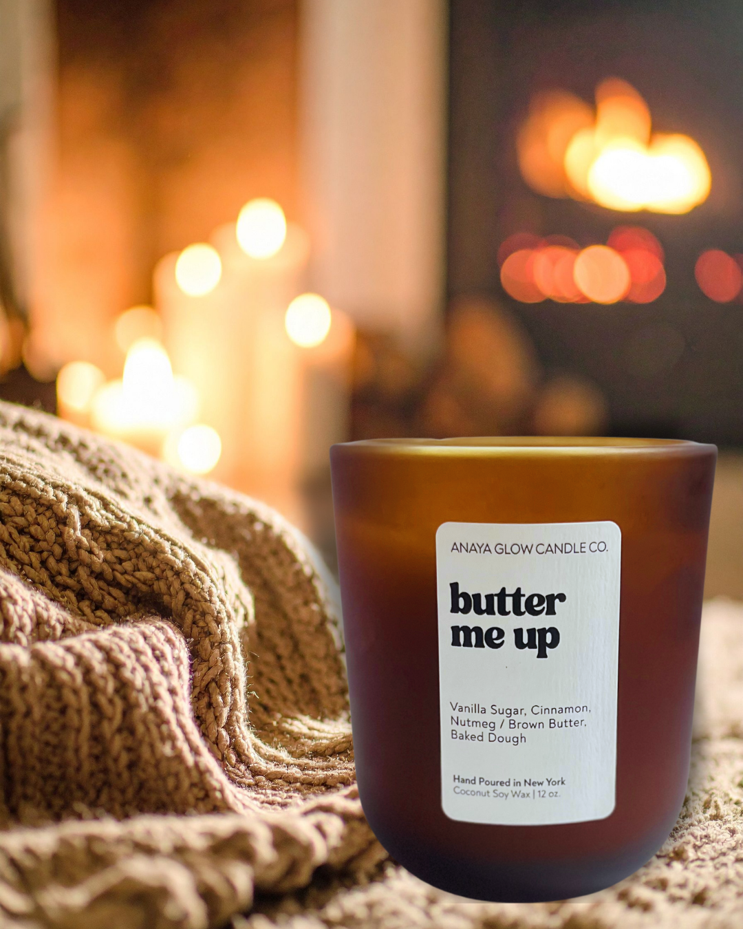 Hand-poured Butter Me Up candle by Anaya Glow Candle Co., set in a warm, cozy space with soft lighting and candles glowing in the background.